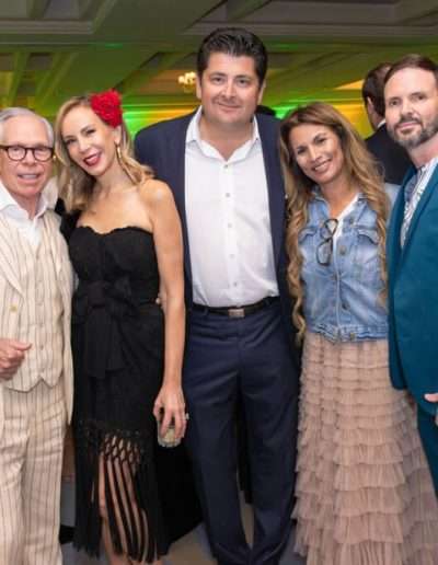 Five adults in formal and semi-formal attire pose together at the Annual Auction & Ball, with vibrant green and yellow lighting illuminating the indoor event in the background.